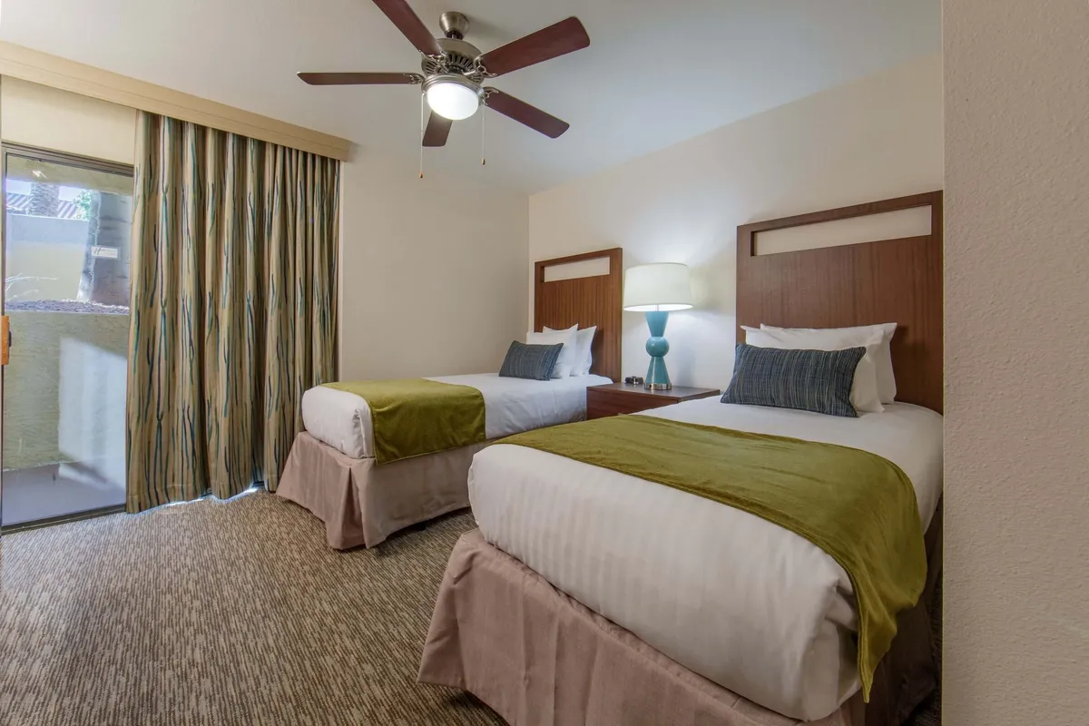 A cozy bedroom with two single beds, accented by colorful curtains and a shared table lamp. The space is filled with natural light, making it ideal for families or friends. The inviting setup emphasizes togetherness and comfort.