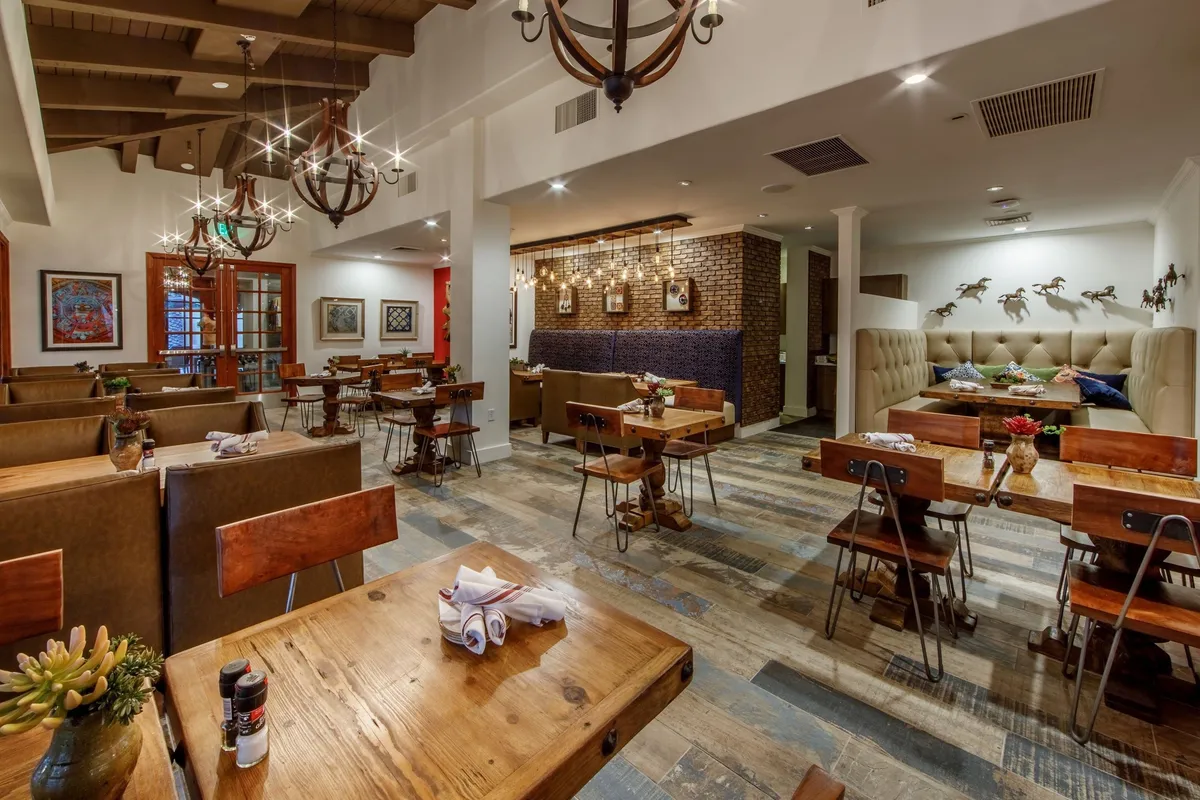 This image showcases a warm and inviting interior space with wooden tables, comfortable seating, chandeliers, and artwork on the walls. The ambiance exudes sociability and relaxation, encouraging gathering and conversation.
