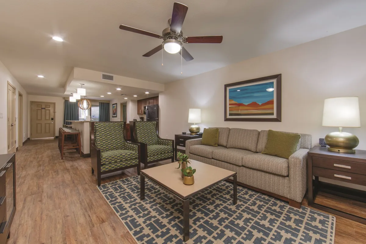 The image showcases the inviting interior of the villa's living room, featuring a plush sofa, two vibrant green chairs, a stylish coffee table, and eye-catching artwork on the wall. The arrangement encourages guests to relax, socialize, and enjoy cozy moments together, with abundant natural light enhancing the welcoming atmosphere.