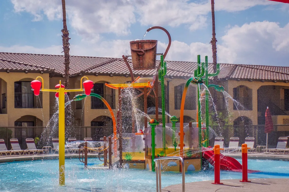 A vibrant pool area with colorful water slides and a splash pad, where children and families are actively playing and having fun. The image captures the excitement and family-friendly vibe of the Splash Canyon water feature, as well as ample poolside relaxation space.