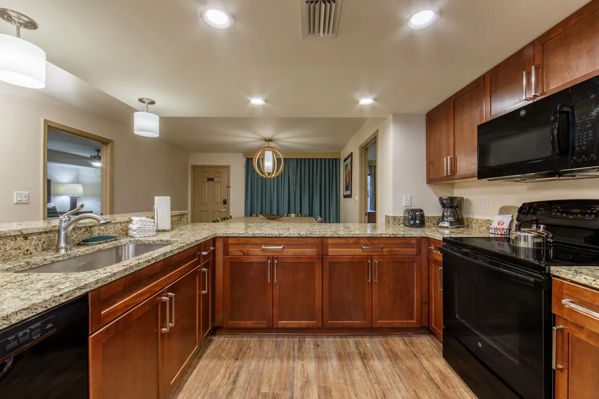 This image showcases a modern villa kitchen with granite countertops, elegant wood cabinetry, and high-end appliances such as a stove, oven, microwave, refrigerator, and dishwasher. The kitchen layout is open and inviting, perfect for preparing meals or gathering with friends and family. The atmosphere feels warm and encourages culinary creativity.