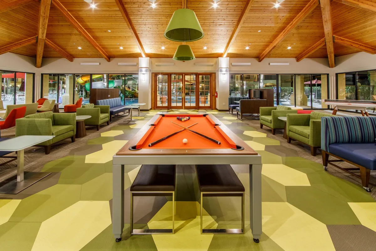 A casual and fun interior scene featuring a pool table, green seating, and decorative lighting. The space is designed for entertainment and relaxation, inviting guests to socialize and enjoy leisure activities together.