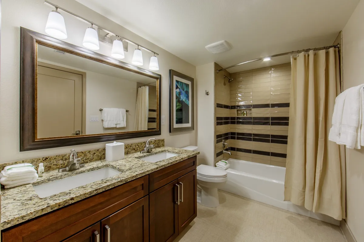 A modern bathroom featuring a double vanity with two sinks, a large mirror, framed artwork, and a bathtub with shower. The room feels refreshing and serene, perfect for both starting the day and winding down at night.