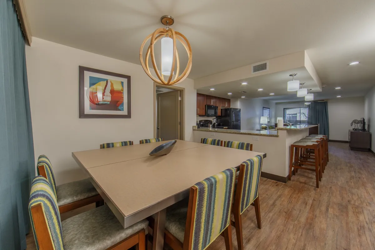 A spacious dining area featuring a large, welcoming dining table set beneath an eye-catching lighting fixture. The kitchen is visible in the background, and tasteful wall art adds a touch of elegance. The scene exudes a sense of togetherness, ideal for family breakfasts, group dinners, and social gatherings.